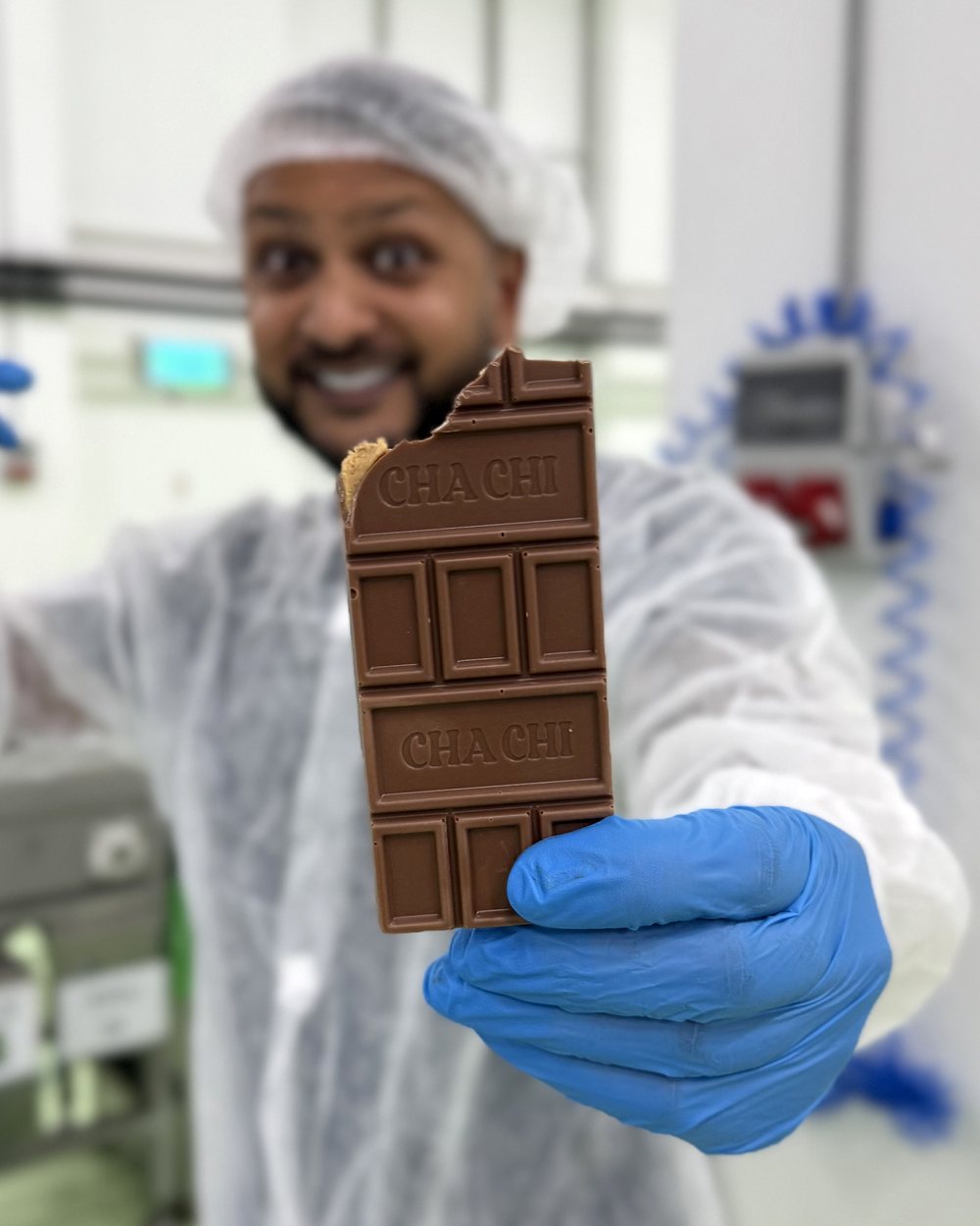Cha Chi Versaci houdt in de fabriek een CHACHI-reep omhoog waar een hap uit is